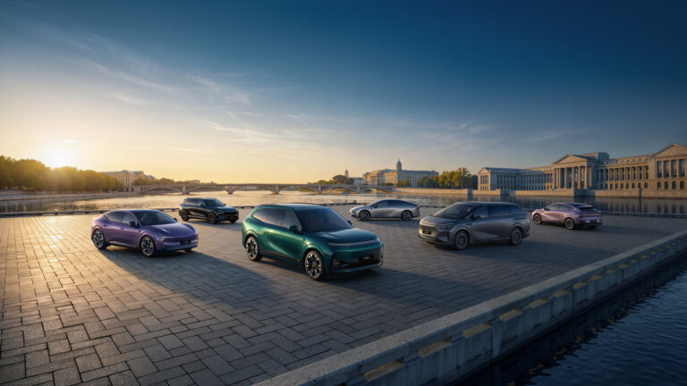 Six XPENG cars in different colours parked on a paved quayside by a river at sunset
