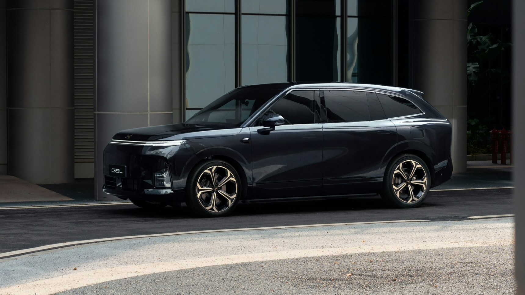 XPENG G9L Black Gold Edition side view with gold-accent wheels in front of a grey building