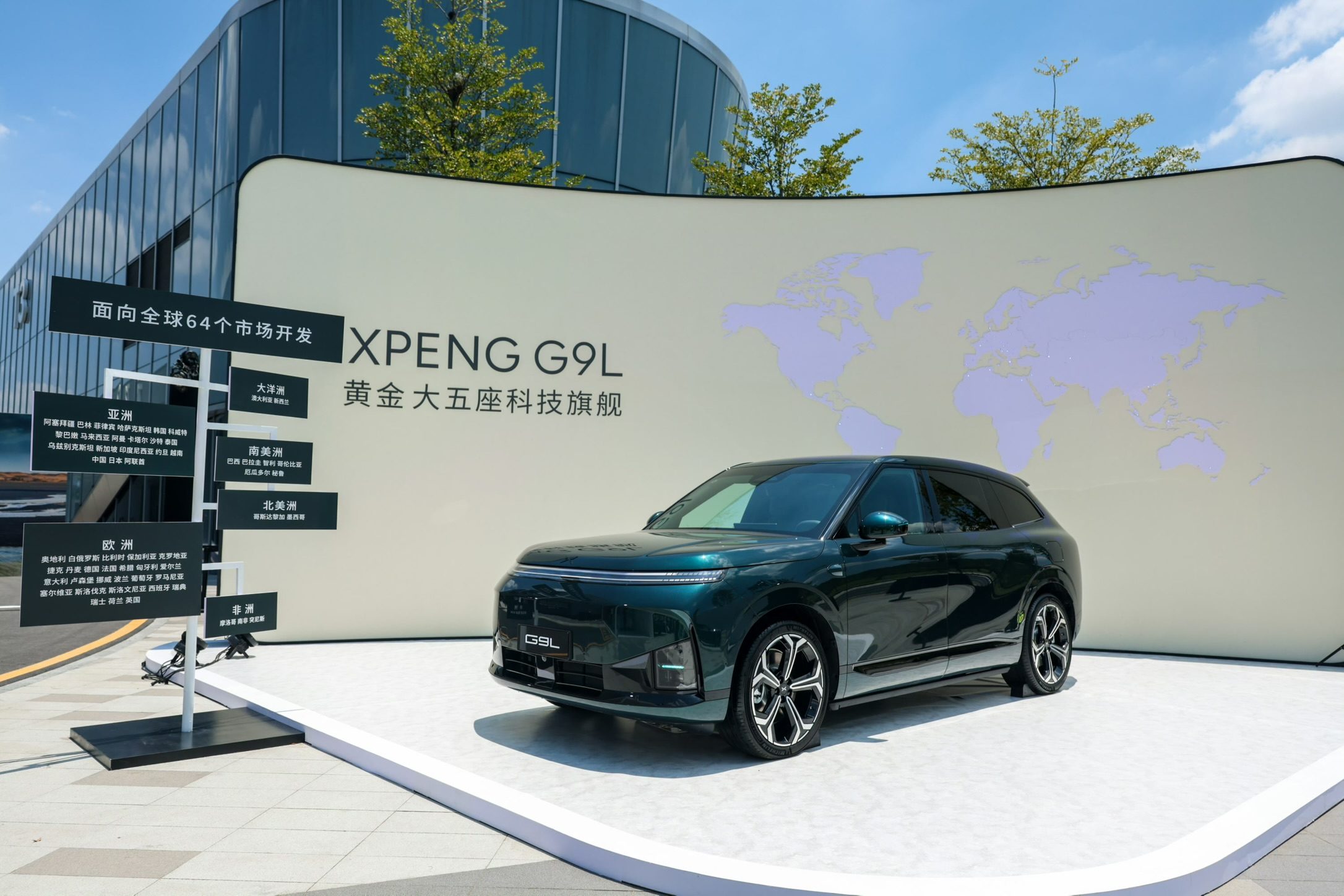 XPENG G9L in Toscana Green beside the Guangzhou stand board listing the 64 launch markets by continent, Denmark in the Europe column