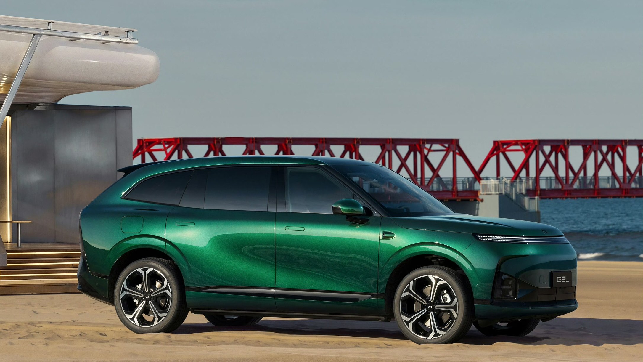 XPENG G9L side profile in Toscana Green on a beach with a red pier in the background