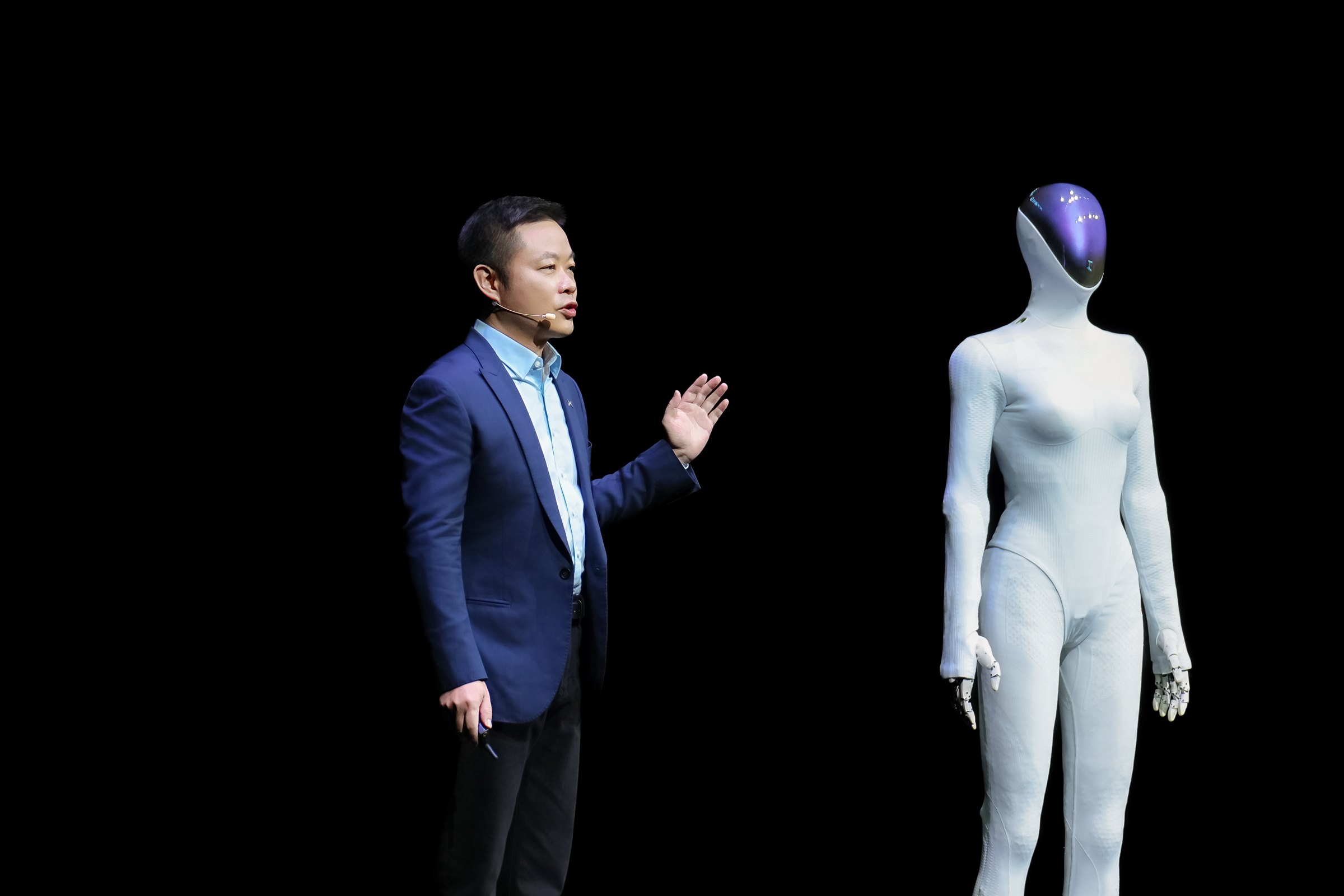 He Xiaopeng on a dark stage beside the white Next-Gen IRON humanoid robot with its dark head screen