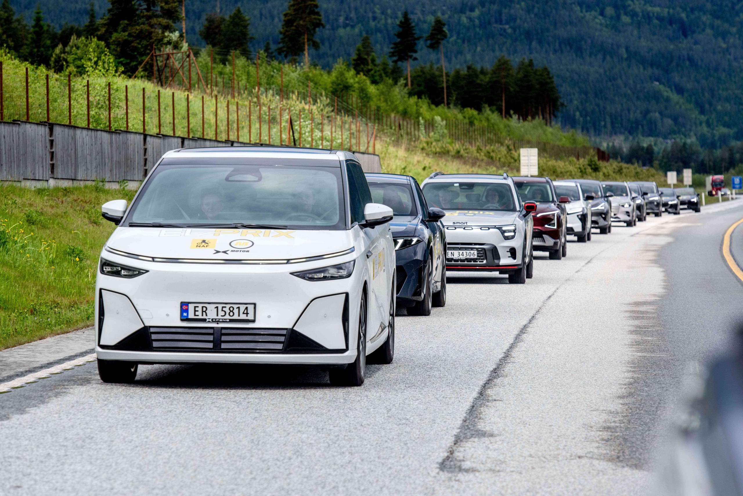White XPENG X9 in El Prix livery leading a convoy of test cars on a Norwegian road