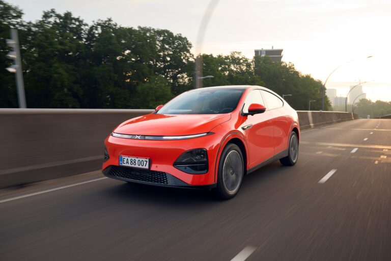 Red XPENG G6 on Danish plates driving on a European road at dusk