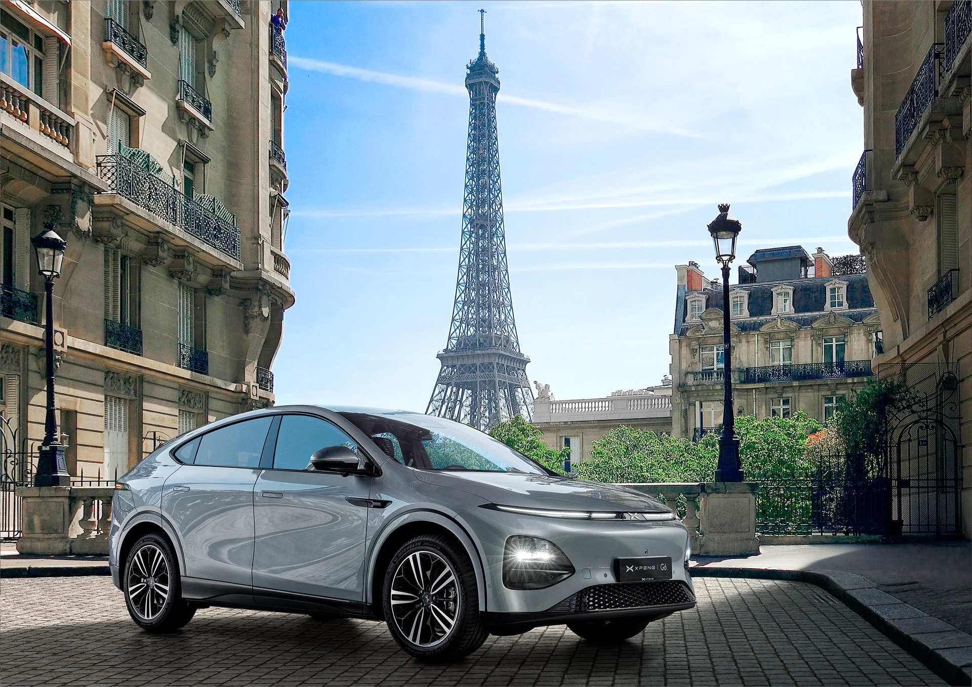 Sølvfarvet XPENG G6 på en brostensgade i Paris med Eiffeltårnet bagved