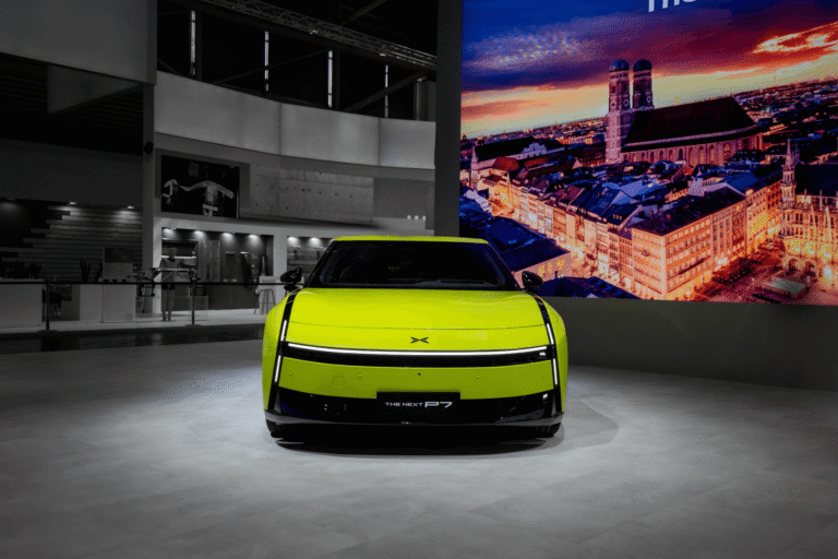 Acid green XPENG Next P7 head-on at IAA Mobility with a lit Munich skyline screen behind