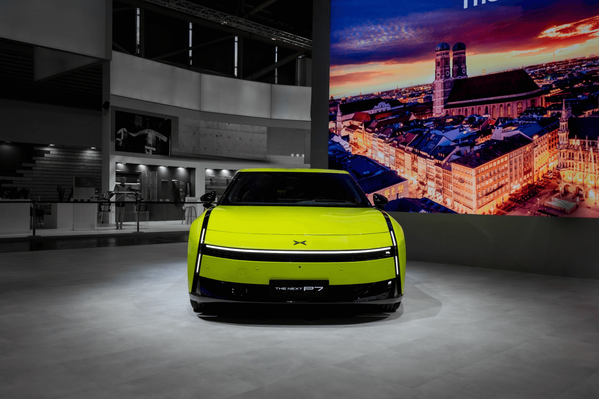 Acid green XPENG Next P7 head-on at IAA Mobility with a lit Munich skyline screen behind