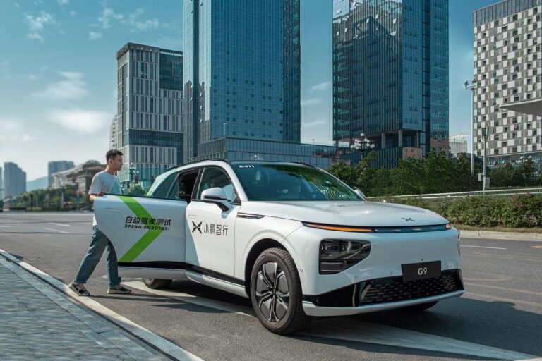 White XPENG G9 robotaxi on a Guangzhou street with the driver's door open and a man stepping away from it