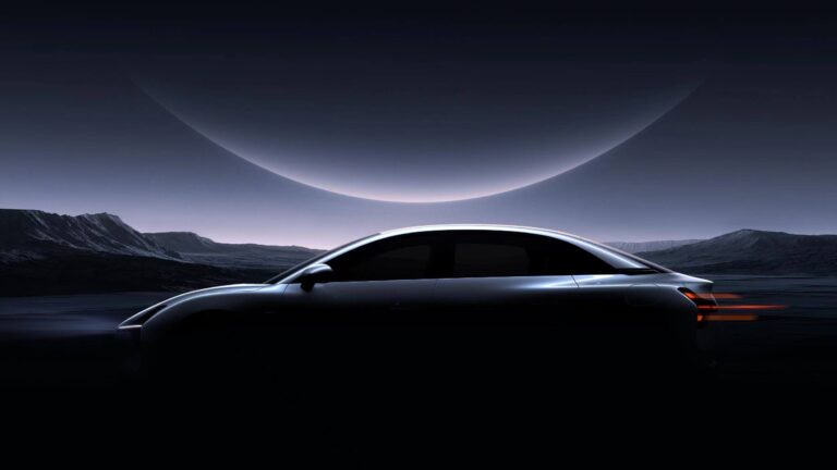 Teaser image of an unbadged silver fastback sedan in profile, lit only along its shoulder line under a crescent-lit sky