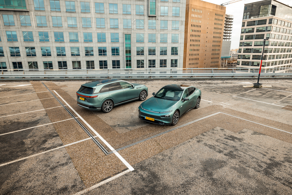 Grøn XPENG G9 og grøn XPENG P7 parkeret på et tagparkeringsdæk med kontorbygninger bagved