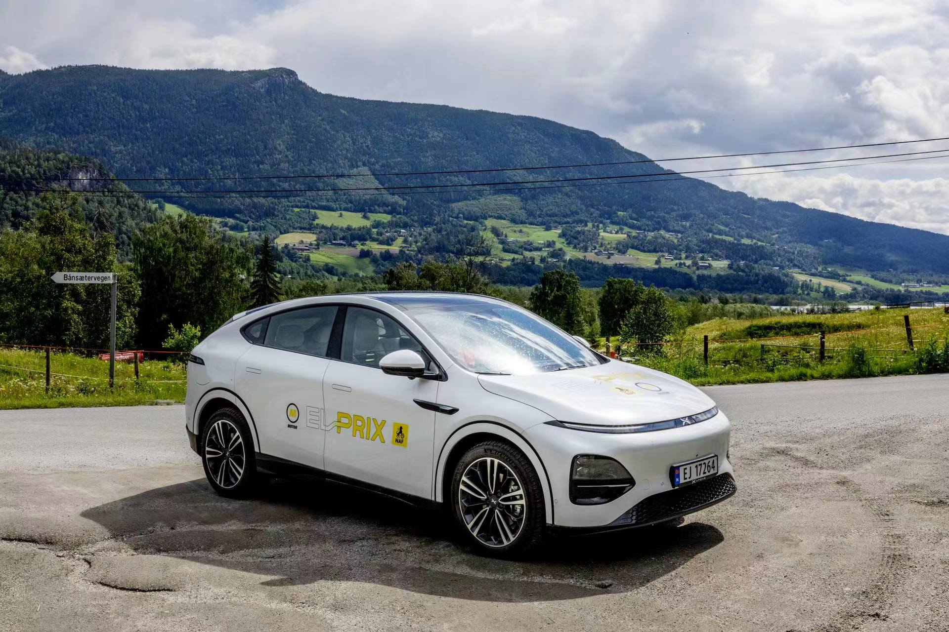 White XPENG G6 with EL-PRIX decals parked on a gravel verge in a green Norwegian valley