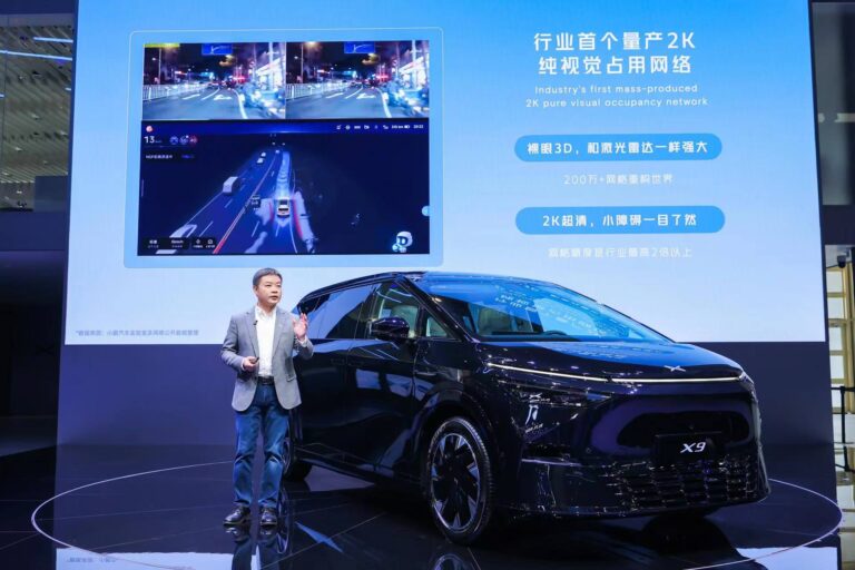 A presenter on stage beside a black XPENG X9 at the Beijing motor show, a large slide behind them
