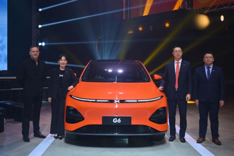 Orange XPENG G6 head-on on a launch stage with four people standing either side of it