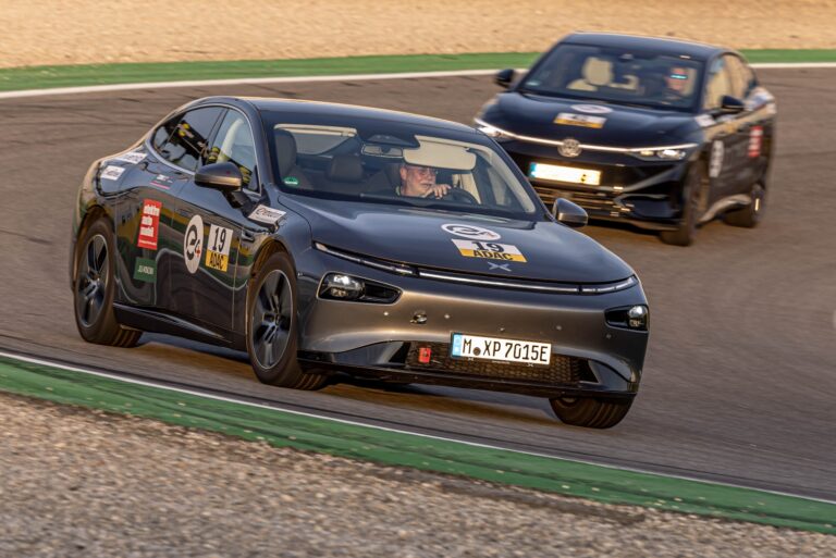 Grey XPENG P7 with race number 19 and ADAC decals cornering on track, a dark rival following