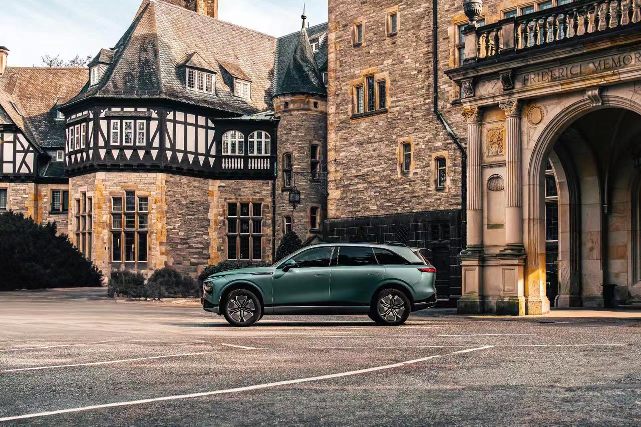 Sage green XPENG G9 in profile in the forecourt of a half-timbered German stone manor