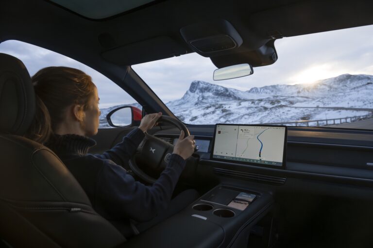 View over a driver's shoulder in an XPENG G9 on a snow-covered mountain road, the centre screen showing navigation