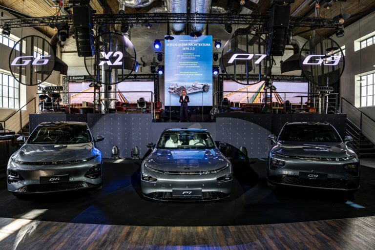 Three silver XPENG cars on a launch stage under illuminated ring letters, a speaker on the podium behind