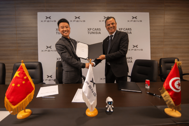 Two men shaking hands over a signed agreement in front of a wall of XPENG and XP Cars Tunisia logos