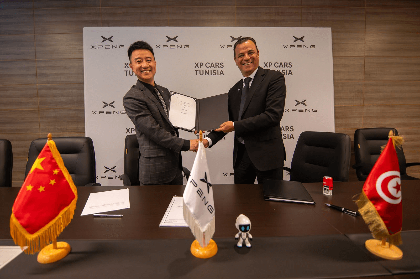 Two men shaking hands over a signed agreement in front of a wall of XPENG and XP Cars Tunisia logos
