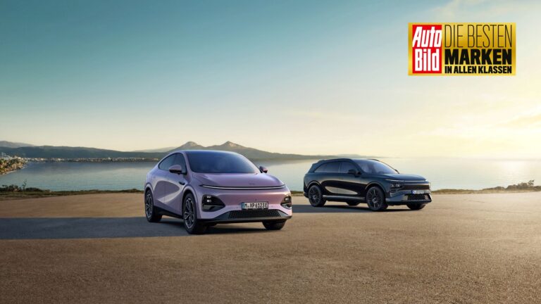 Pale lilac New XPENG G6 and a black New G9 on a coastal apron at sunset, with an Auto Bild award badge in the corner