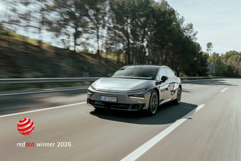Grey XPENG P7+ driving towards the camera on a tree-lined motorway, with a Red Dot winner badge in the lower left