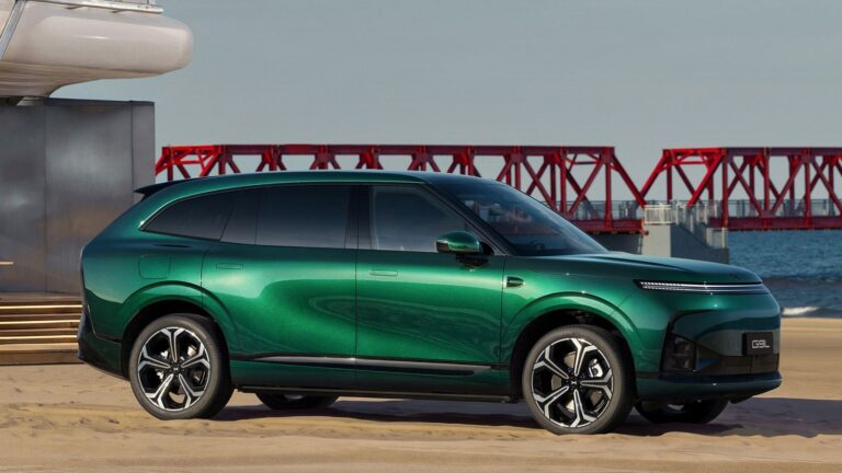 A green XPENG G9L in side profile on a beach in front of a red steel bridge