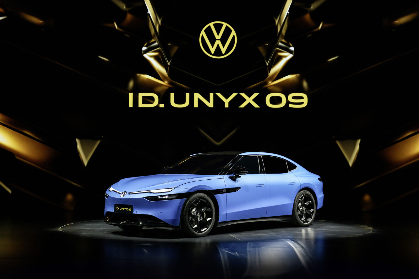 Blå Volkswagen ID. UNYX 09 sedan set skråt forfra på en scene med modelnavnet i baggrunden