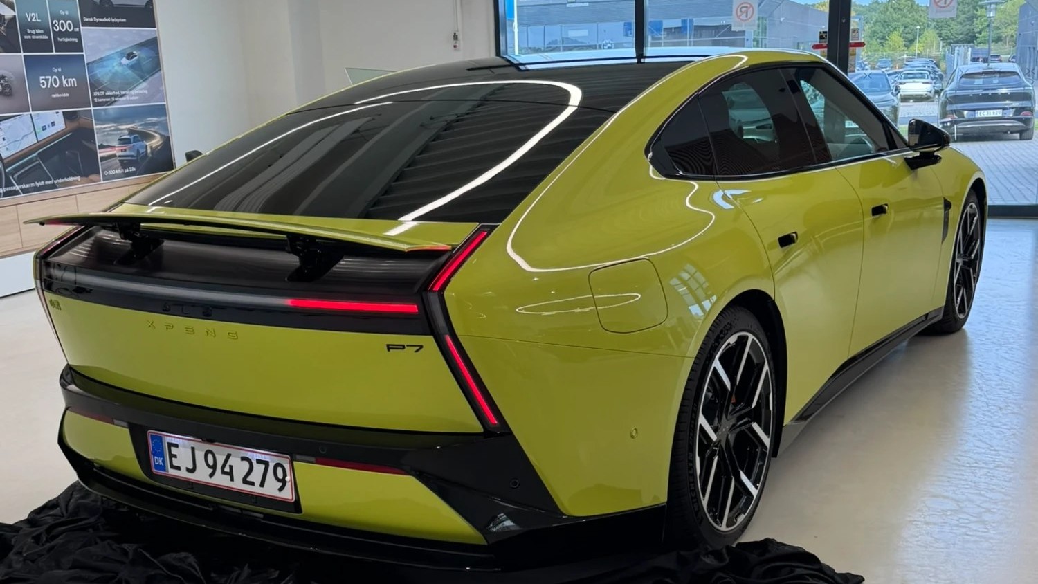 XPENG New P7 in Rhythm Yellow on Danish plates in the XPENG Danmark showroom, rear three-quarter with the rear wing raised
