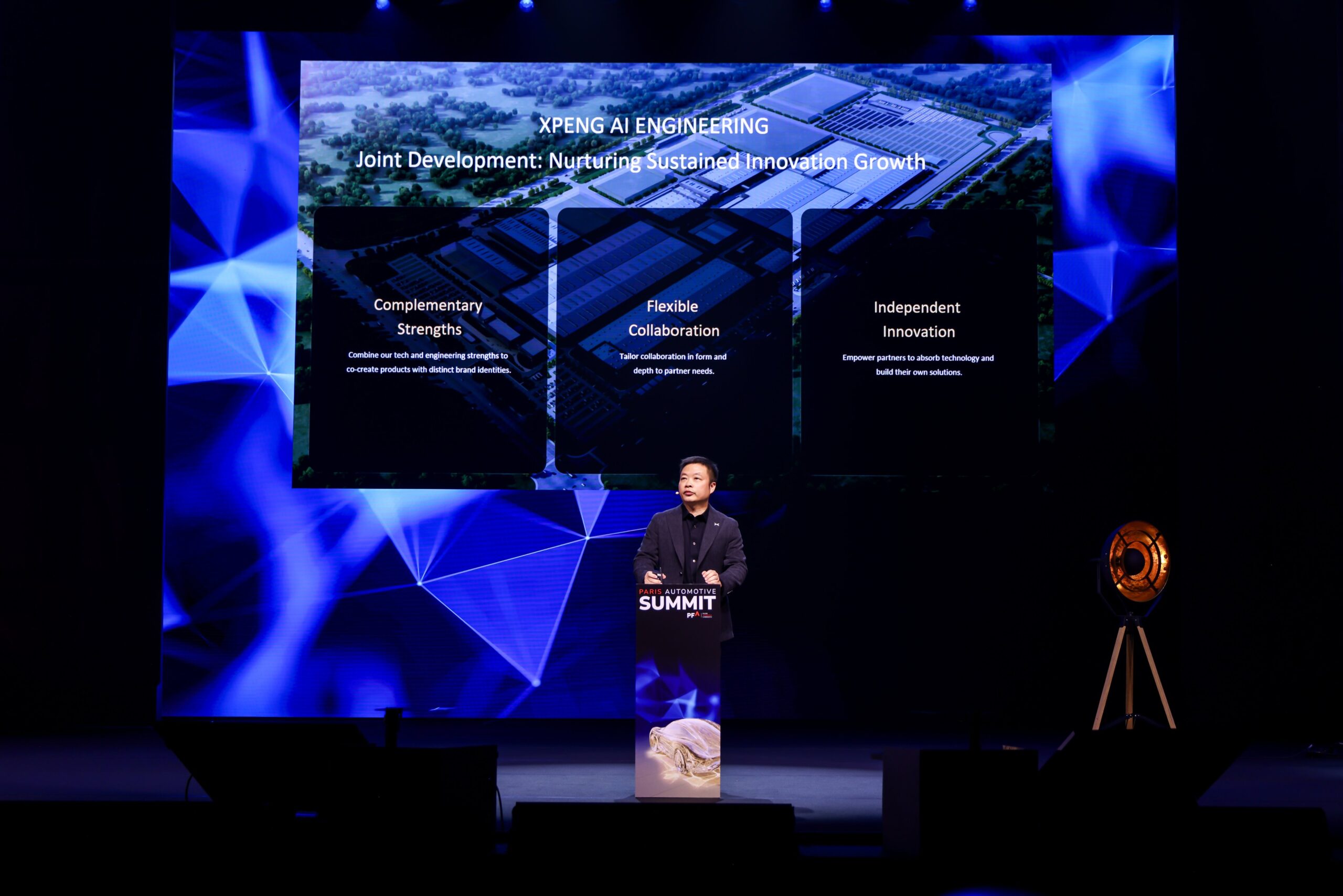 He Xiaopeng på talerstolen ved Paris Automotive Summit foran et slide med overskriften XPENG AI Engineering og tre felter: Complementary Strengths, Flexible Collaboration og Independent Innovation