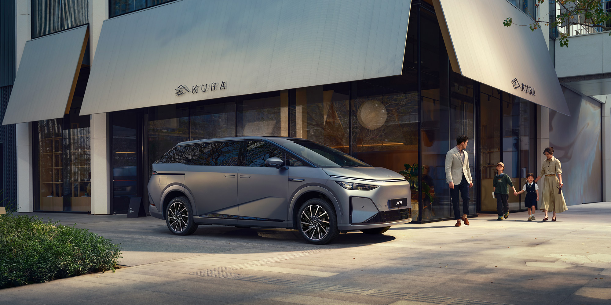 XPENG X9 parked outside a city shop, a family walking past